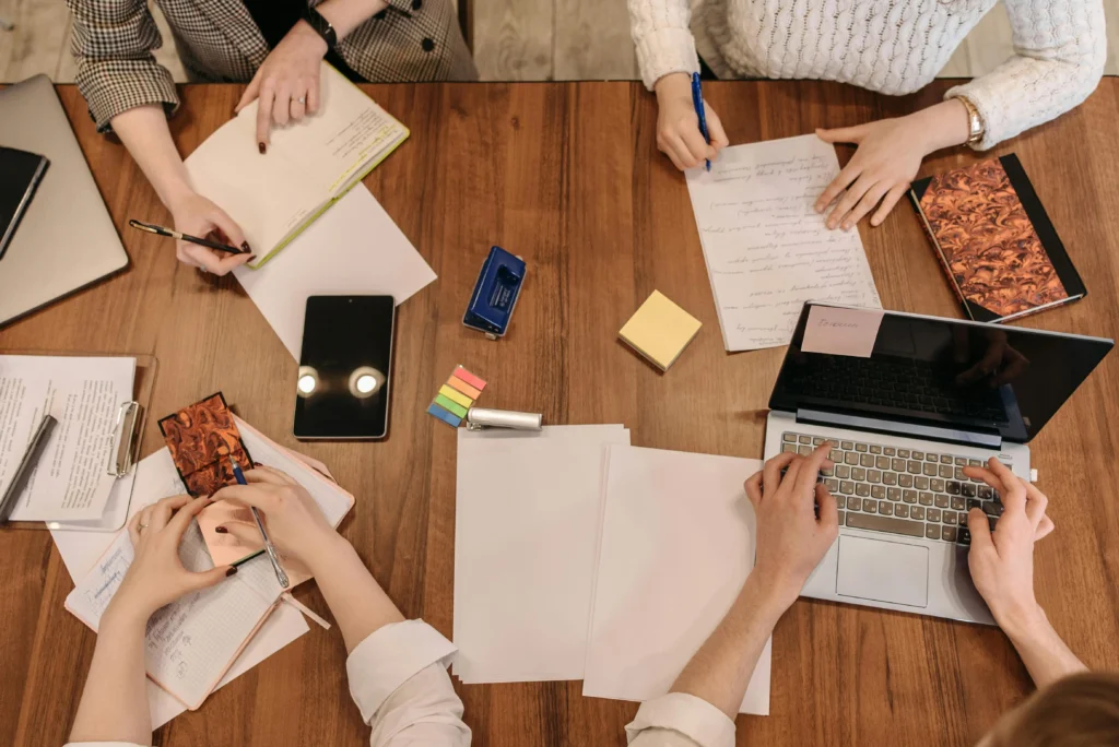 Top-down perspective of individuals engaged in work at a table, focused on their laptops and sharing ideas.