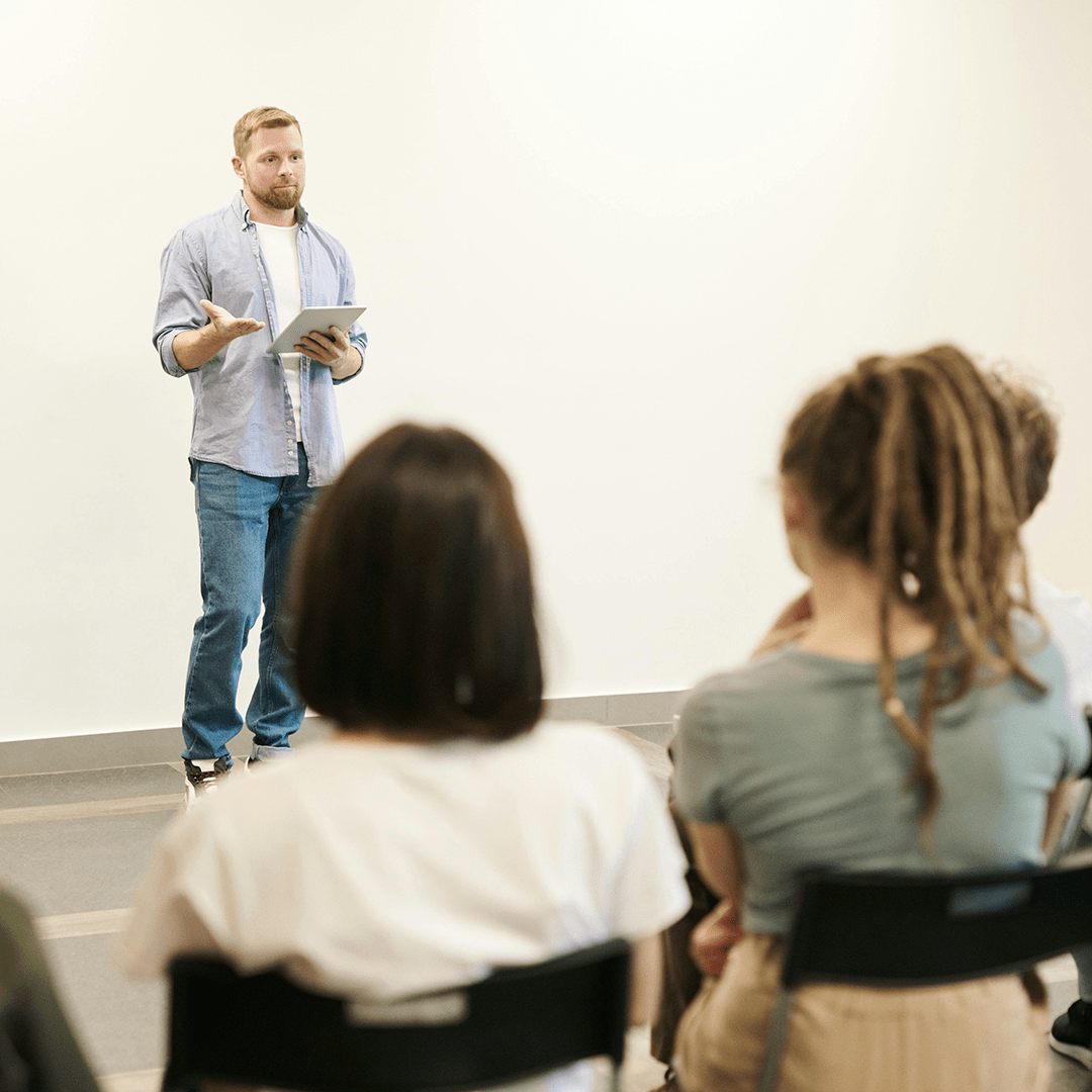A man stands confidently in front of a group of attentive people, engaging them with his presentation.