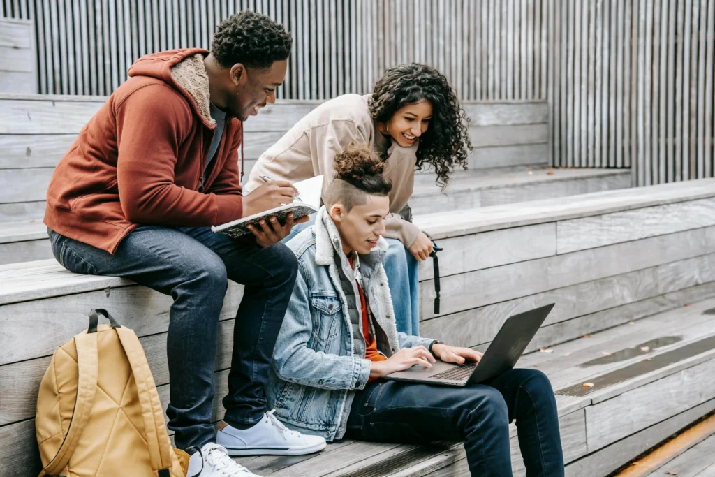 Three students on outdoor steps, each using a laptop, appearing to work together or study.
