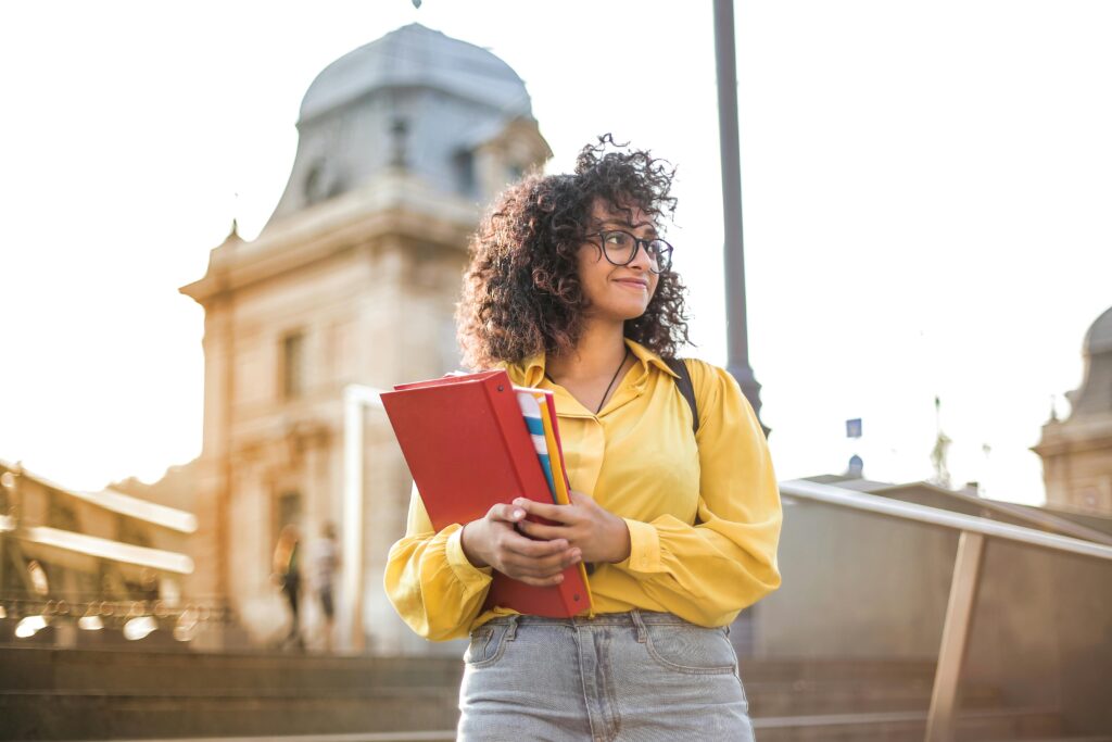 A woman with glasses in a yellow shirt poses on a staircase, showcasing her casual style.
